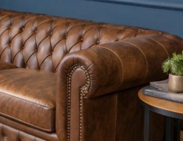 Close view of hand-tied deep buttoning and a rolled arm on a tan leather Chesterfield sofa with brass nail-head trim