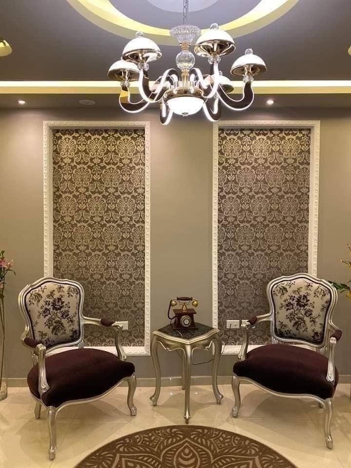 Pair of carved armchairs and a small round side table under a chandelier, between two lattice-screen panels