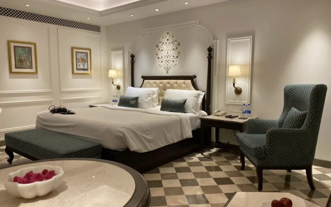 Hotel guest room with an upholstered headboard, bed-end bench, wingback armchair and round table