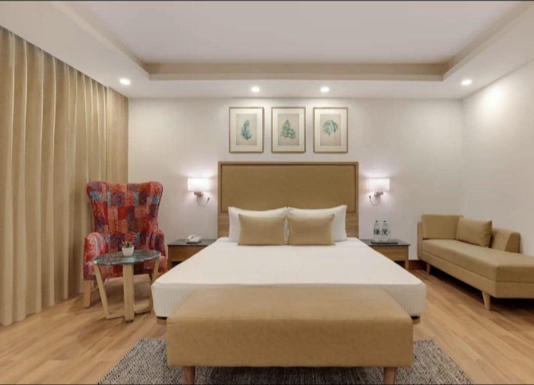 Hotel guest room with an upholstered bed-end bench, patchwork wingback armchair and a daybed sofa