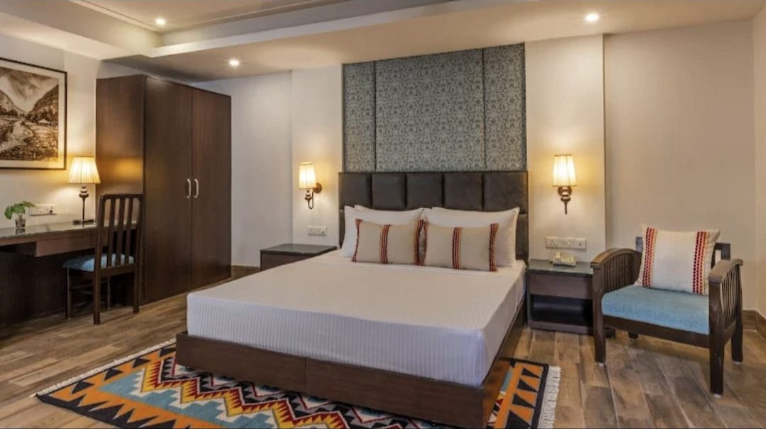 Hotel guest room with a panelled headboard wall, wall lights, bedside tables, desk and a wooden armchair