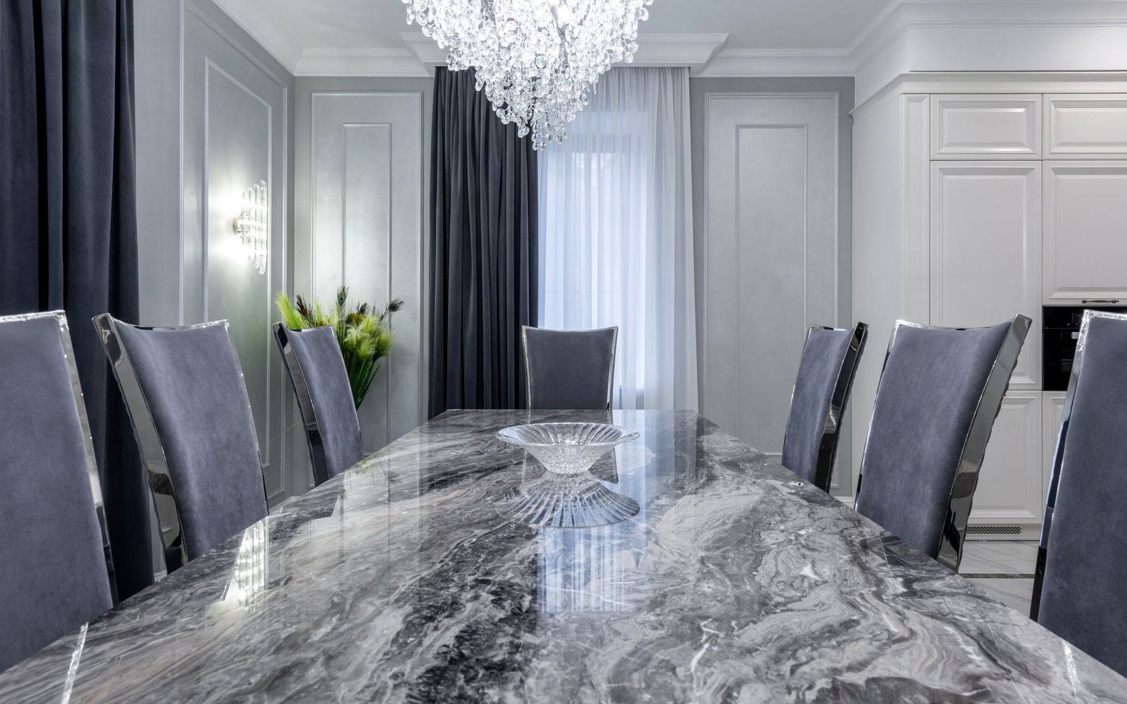 Long polished grey marble dining table with velvet chairs and a crystal chandelier in a panelled dining room