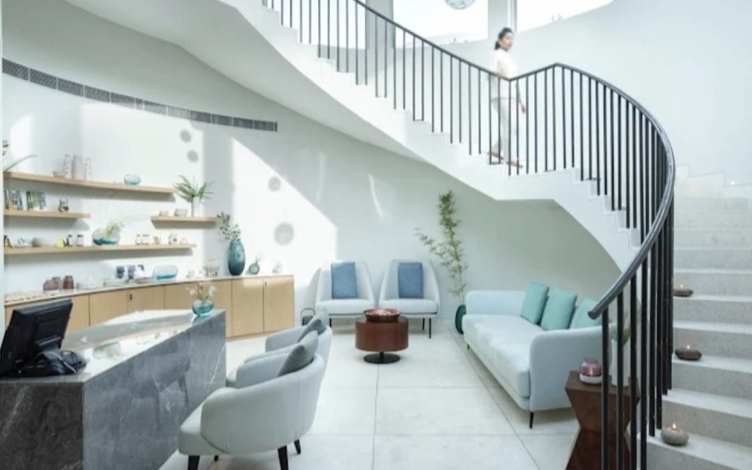 Reception counter in grey stone with lounge seating and a curved staircase in a bright lobby