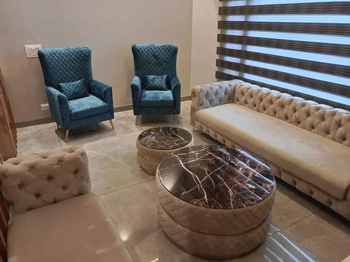 Pair of round marble-topped nesting coffee tables in front of a tufted sofa with blue velvet wingback chairs