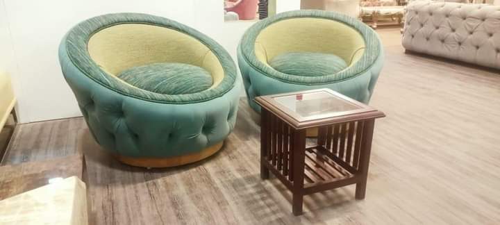 Small wooden side table with a glass top between two round velvet tub chairs