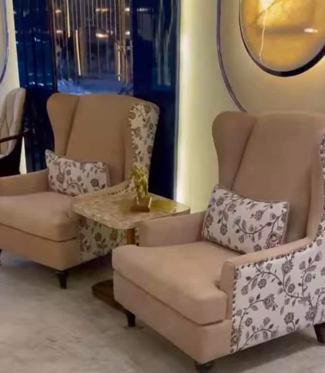 Pair of wingback armchairs in blush fabric with floral-patterned sides and a small side table between them