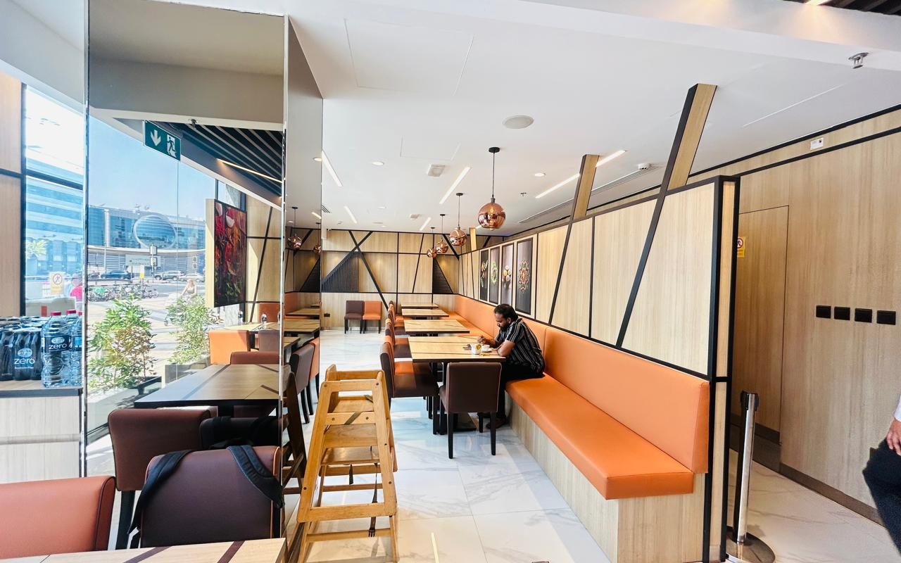 Open-plan workspace with built-in bench seating along a window, communal tables and pendant lights
